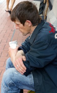 man, asleep, asking for money with a cup in his hand.